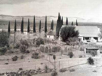 The werf at Rondawel, looking across the garden to the house: a long white gabled homestead under a corrugated-iron...