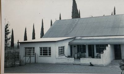 The Rondawel homestead from the yard: a long white house with a steep corrugated-iron roof over the older core and a...
