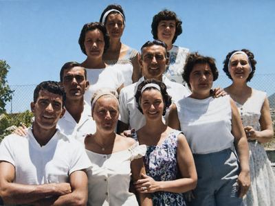 Ten grown brothers and sisters crowded together in the sun against a wire fence, the eldest at the back. FRANS...