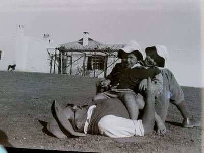 Hennie Oosthuizen lying full length on the bare ground in shirtsleeves, his hat beside him, with two small boys in...