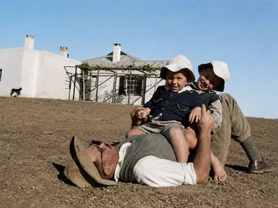 Hennie Oosthuizen lying full length on the bare ground in shirtsleeves, his hat beside him, with two small boys in...