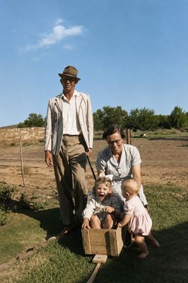 Hennie Oosthuizen in a hat and dark glasses pulling a home-made box cart with a small girl sitting in it, laughing;...
