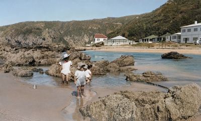 The rock pools at Herolds Bay at low tide, with three children in sun-hats wading in a shallow pool among the rocks....
