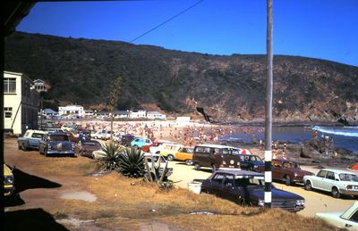 Herolds Bay in high summer, shot from under the eaves of a house above the beach. The sand is packed with bathers to...