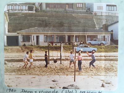 A volleyball game on the sand at Herolds Bay in front of a long single-storey house with a tiled roof and a run of...