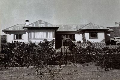 The homestead at Vredendal seen across the garden: a long single-storey house with hipped corrugated-iron roofs and...